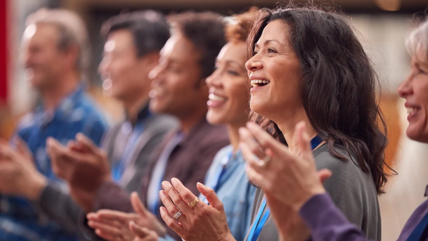 A group of people are standing side by side and happily clapping.