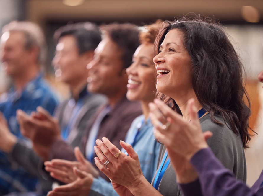 A group of people are standing side by side and happily clapping.