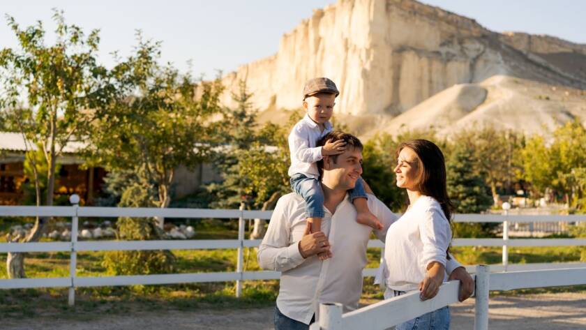 Man, woman, and a child on a family vacation standing on a trail next to a white picket fence. 