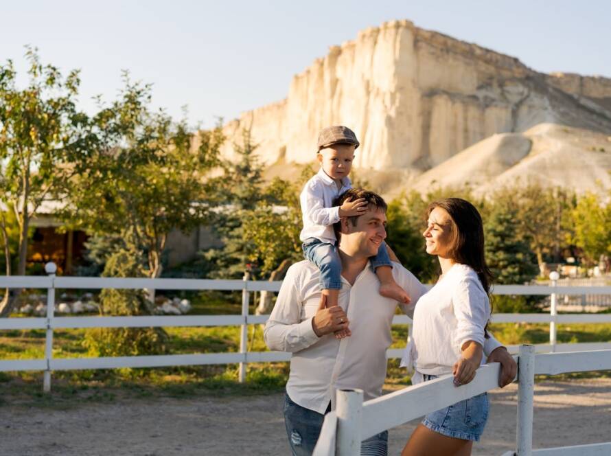 Man, woman, and a child on a family vacation standing on a trail next to a white picket fence. 