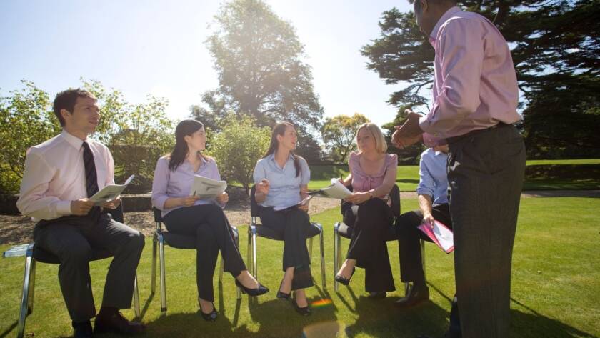 Businesspeople sit outside and discuss a client during a corporate event.