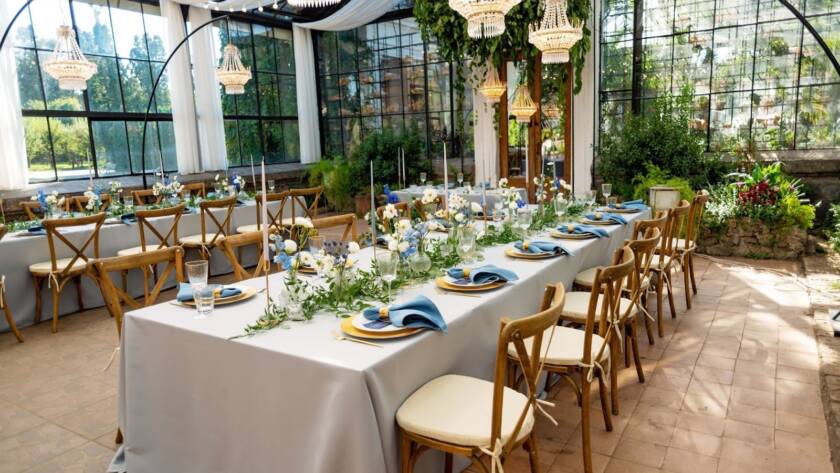 A venue rental set up with tables, blue napkins, gold cutlery, crystal, fresh flowers and candles.