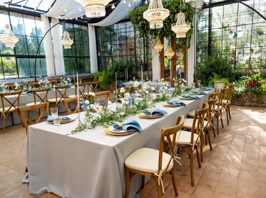A venue rental set up with tables, blue napkins, gold cutlery, crystal, fresh flowers and candles.