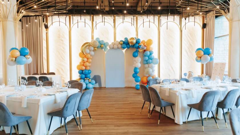 An elegant private event venue featuring a custom balloon arch and coordinated table settings