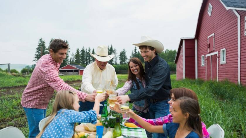 Multi-generation family celebrating a joyful family vacation, toasting glasses together outside a rustic barn during sunset.