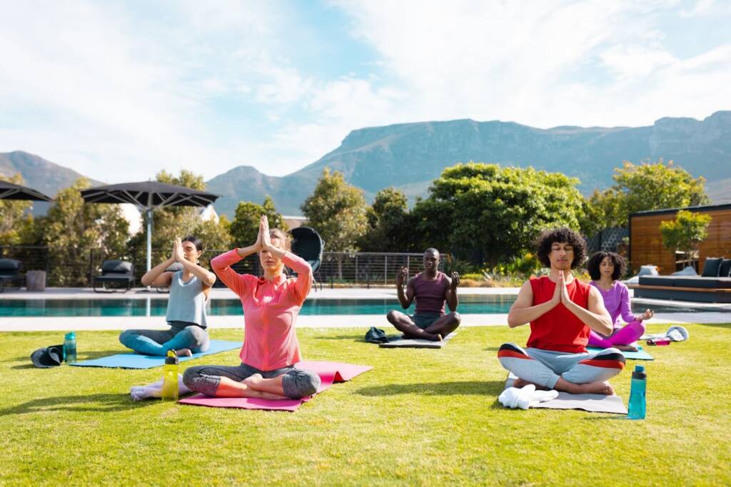 Diverse group of friends practicing yoga and meditation in a garden with a pool