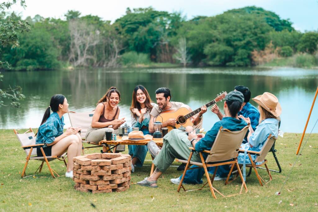 Church retreat participants gather by the lakeside, playing guitar, singing worship songs, and sharing joyful moments