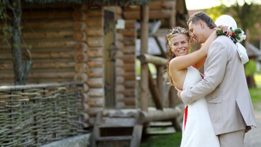 Bride and groom embracing for a photo beside a rustic log cabin after their ranch wedding ceremony