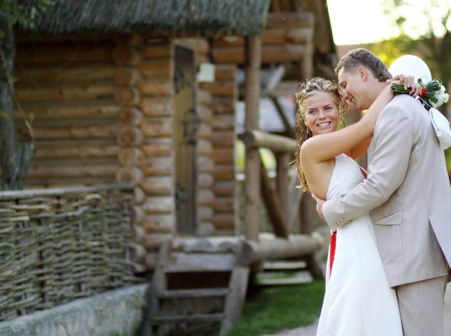 Bride and groom embracing for a photo beside a rustic log cabin after their ranch wedding ceremony