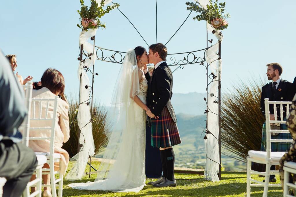 Bride and groom exchanging vows beneath a flower-covered arch during an outdoor ranch wedding ceremony